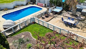 A backyard with a swimming pool, a covered patio area, and a fenced garden.