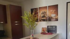 Una cocina moderna con encimera blanca, dos taburetes de bar, una planta decorativa y un cartel en la pared que indica disponibilidad de WiFi.