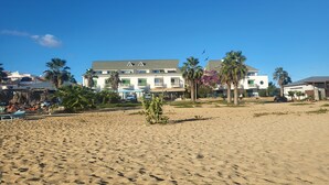 Un hotel frente a la playa con varios balcones, palmeras y una playa de arena.
