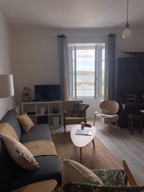 Un salon comprenant un canapé, des fauteuils, une table basse, un téléviseur et une vue sur l’eau.