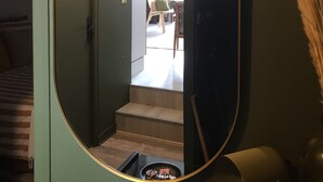 Un pasillo con un espejo grande que refleja una habitación con cama, sillón y escalera.