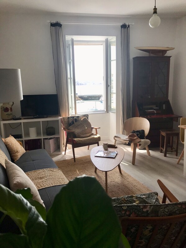 Un salon comprenant un canapé, des fauteuils, une table basse, un téléviseur et une bibliothèque.