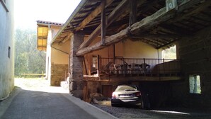 Una stretta strada conduce a un edificio con facciata in pietra e travi in legno. Un'auto è parcheggiata di fronte.