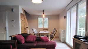 Un accogliente soggiorno con una panca in legno, un divano con cuscini, un tavolo da pranzo con sedie e vista sull'esterno attraverso ampie finestre.