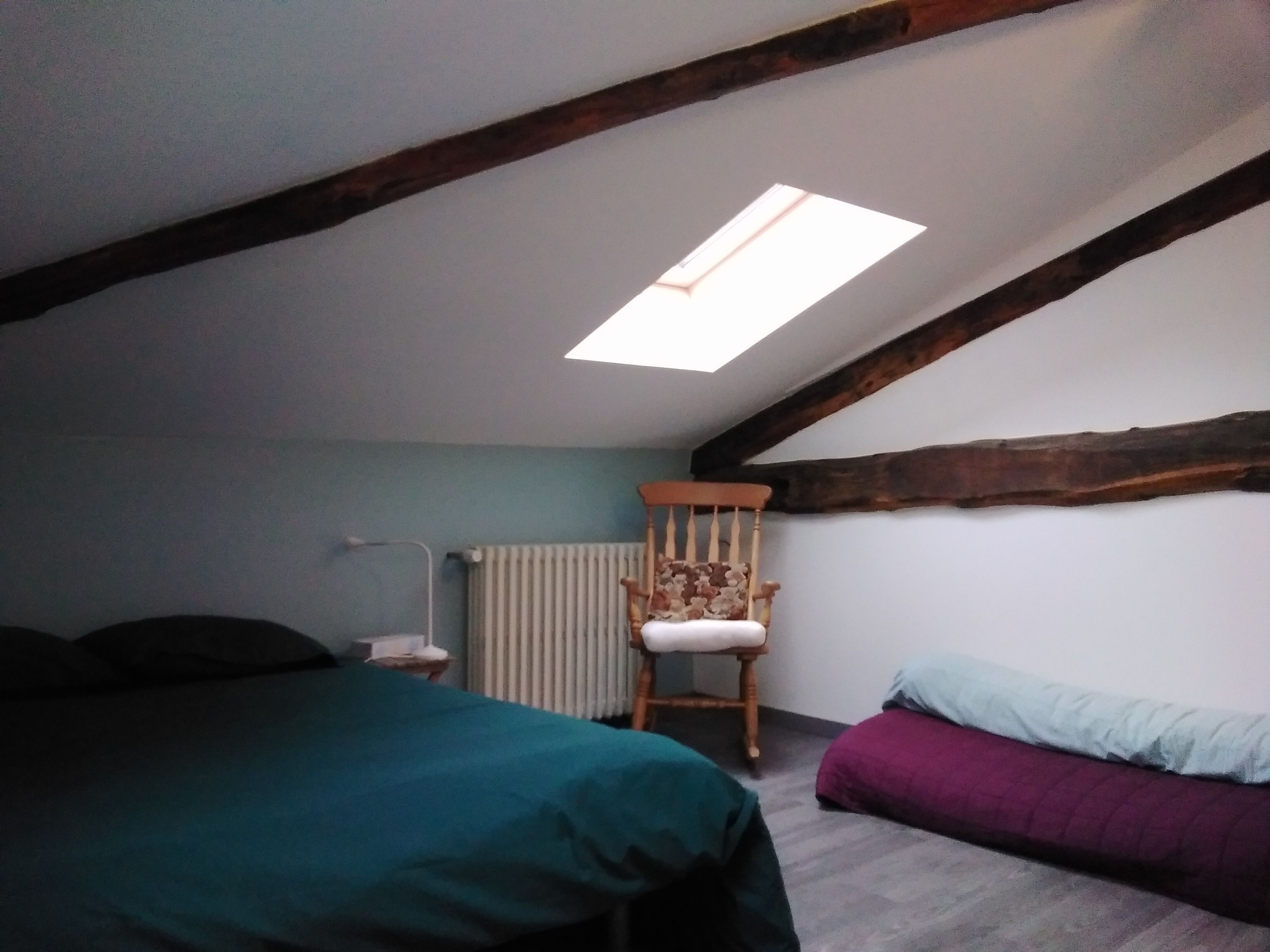 Ein Schlafzimmer mit schrägem Dach, einem Holzstuhl, einem Bett und einer Heizung.
