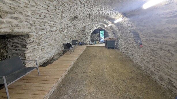 Un interno caratterizzato da una parete in pietra, panche in legno e un pavimento in ghiaia.