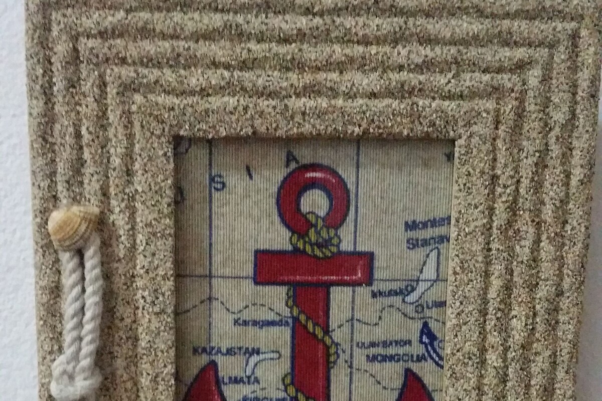 A framed nautical-themed artwork with an anchor and a ship, surrounded by rope and a starfish.