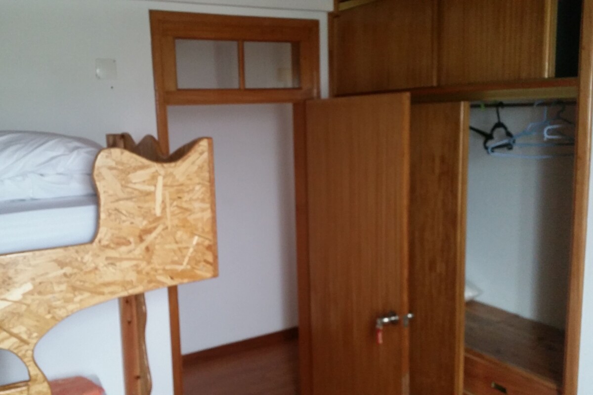 A small room with a bunk bed, wooden wardrobe, and a small desk.