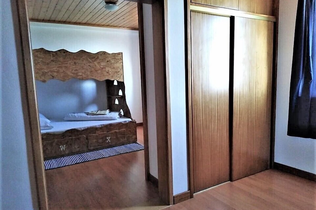 A bedroom with a wooden headboard, a bed with white linens, a nightstand, and a wardrobe with sliding doors.