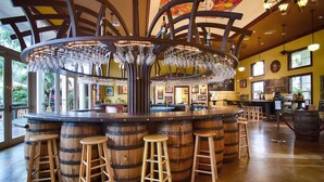 A bar area with a central circular bar surrounded by wooden barrels and stools. - Stay in our cozy tiny house inside an award-winning garden in SW Miami-Dade’s beautiful Redlands! (Homestead)