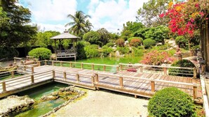 A wooden bridge over a pond with a gazebo and lush greenery. - Stay in our cozy tiny house inside an award-winning garden in SW Miami-Dade’s beautiful Redlands! (Homestead)