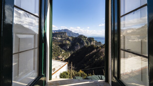 Blick aus einem Fenster auf eine Berglandschaft und ein Gewässer in der Ferne.