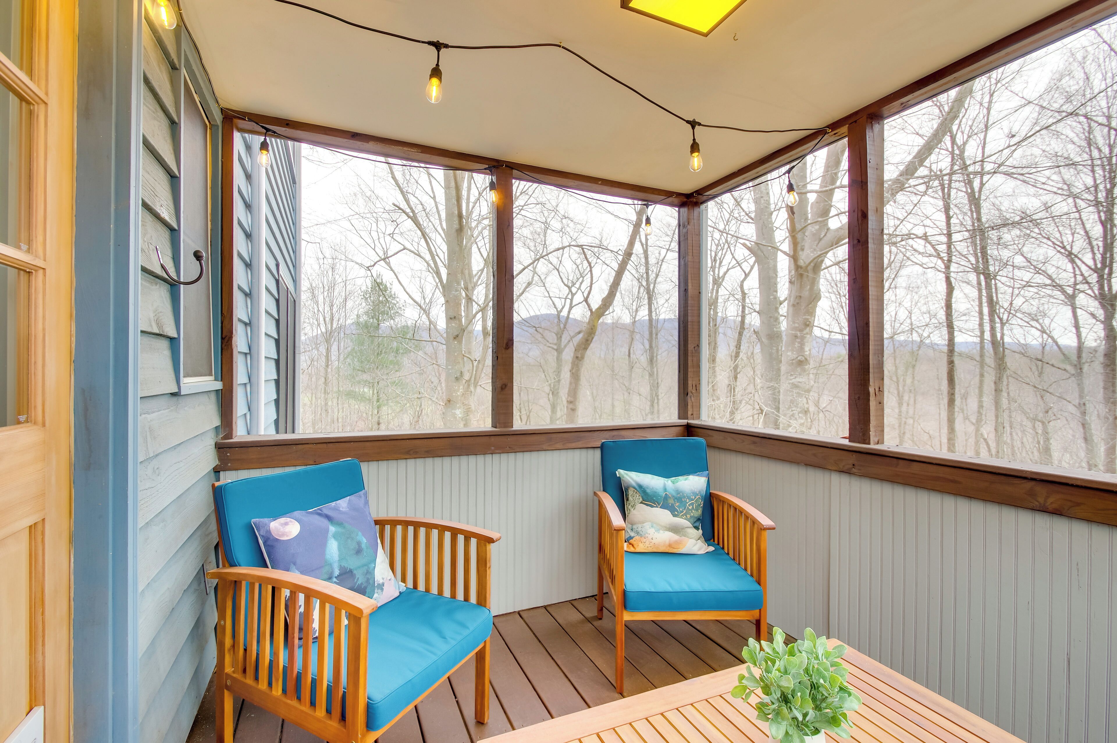 Eine überdachte Veranda mit zwei Holzstühlen und einem Tisch, großen Fenstern und einer Lichterkette.