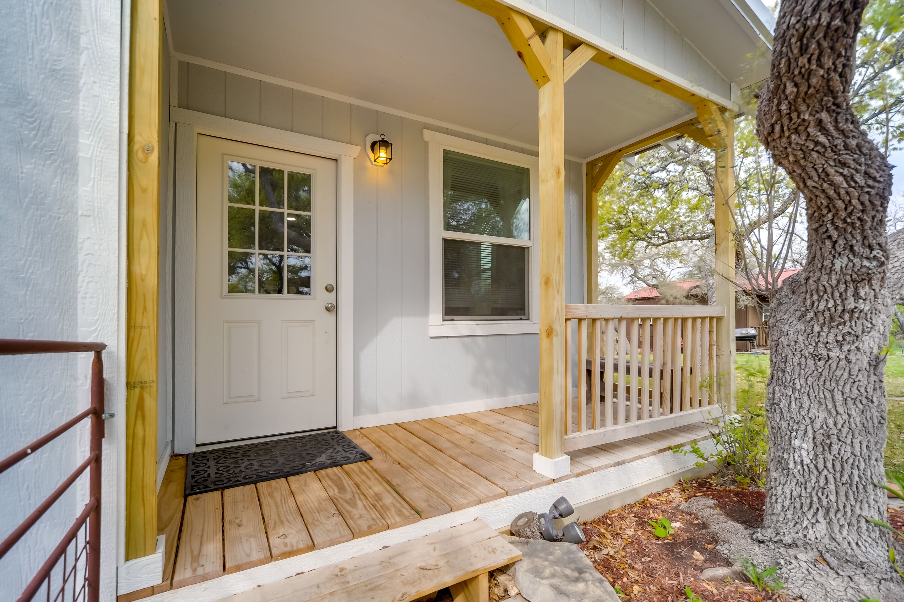 A wooden porch with a white door and a window, a bench, and a tree.