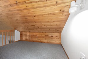 A room with a sloped ceiling, wooden paneling, a carpeted floor, a white wall, and a white staircase.