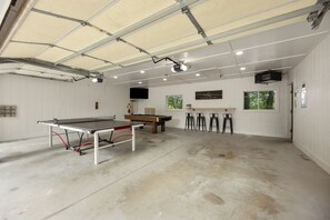 A spacious indoor area with a ping pong table, a pool table, and bar stools. - Lake Montcalm Waterfront Retreat - Beach, Hot Tub, Game Room (Six Lakes)