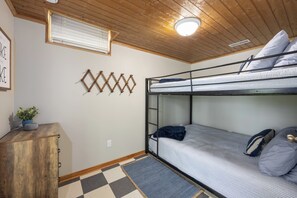 Une chambre avec un lit superposé, un sol à carreaux, un bureau avec une plante et un luminaire fixé au mur.