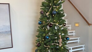 Ein Weihnachtsbaum mit Schmuck und Lichter, eine Treppe und ein gerahmtes Bild an der Wand.