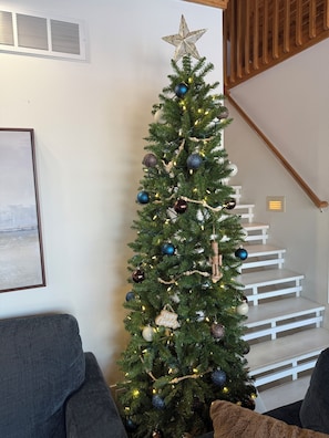 Un sapin de Noël décoré d’ornements et de guirlandes lumineuses, un escalier et un tableau encadré accroché au mur.
