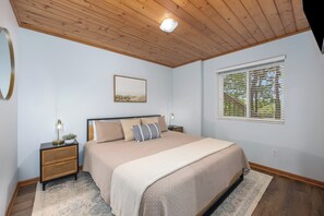 A bedroom with a bed, bedside tables, a nightstand, a window with blinds, and a ceiling light. - Lake Montcalm Waterfront Retreat - Beach, Hot Tub, Game Room (Six Lakes)