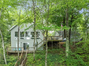 A two-story house with a wooden deck and a staircase leading to the upper level. - Lake Montcalm Waterfront Retreat - Beach, Hot Tub, Game Room (Six Lakes)