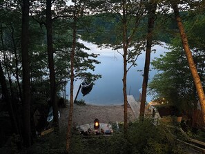 A lakeside cabin with a dock extending into the water, surrounded by tall trees. - Lake Montcalm Waterfront Retreat - Beach, Hot Tub, Game Room (Six Lakes)