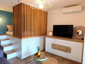 A modern living space with a wooden slatted partition, a flat-screen TV, and a small round table with a pineapple centerpiece.