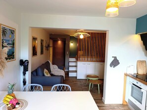 A cozy living room with a sofa, a dining table with chairs, a kitchen area with a stove, and a staircase leading to another level. - Studio 56, Cosy design apartment in Étang-Salé (L'Étang-Salé)