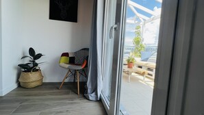 Un balcón con una silla, una planta en maceta y vista al mar.