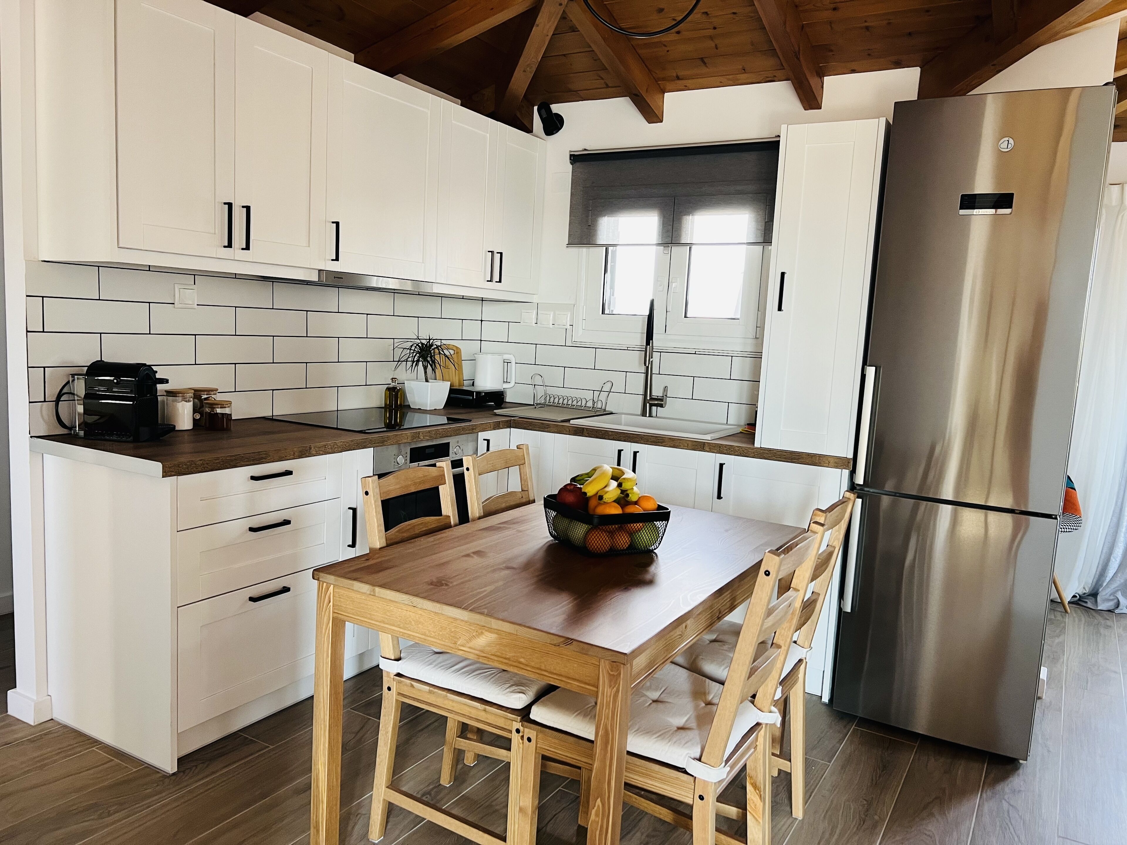 Une cuisine moderne avec des meubles blancs, un plan de travail en bois, un réfrigérateur en acier inoxydable et une table à manger avec des chaises.