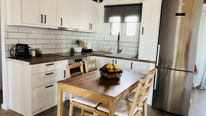 Una cocina moderna con armarios blancos, encimera de madera, refrigerador de acero inoxidable y una mesa de comedor con sillas.