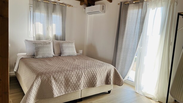 Un dormitorio con cama, cortinas, equipo de aire acondicionado y piso de madera.