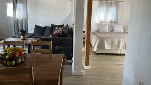 Un espacio habitable moderno y de planta abierta, con techo de madera, una zona de comedor con una cesta de fruta, un sofá con cojines y una cama con colcha acolchada.