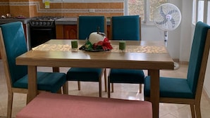 Un área de comedor con una mesa, sillas, un banco, una cocina al fondo y un ventanal con vistas a zonas verdes.