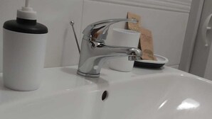 Un lavabo con grifo cromado, dispensador de jabón y un pequeño recipiente.