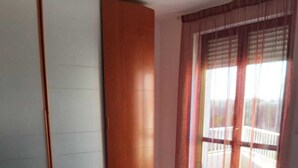 Habitación de hotel con cama, mesita de noche, lámpara, ventana con cortinas y vista a un balcón.