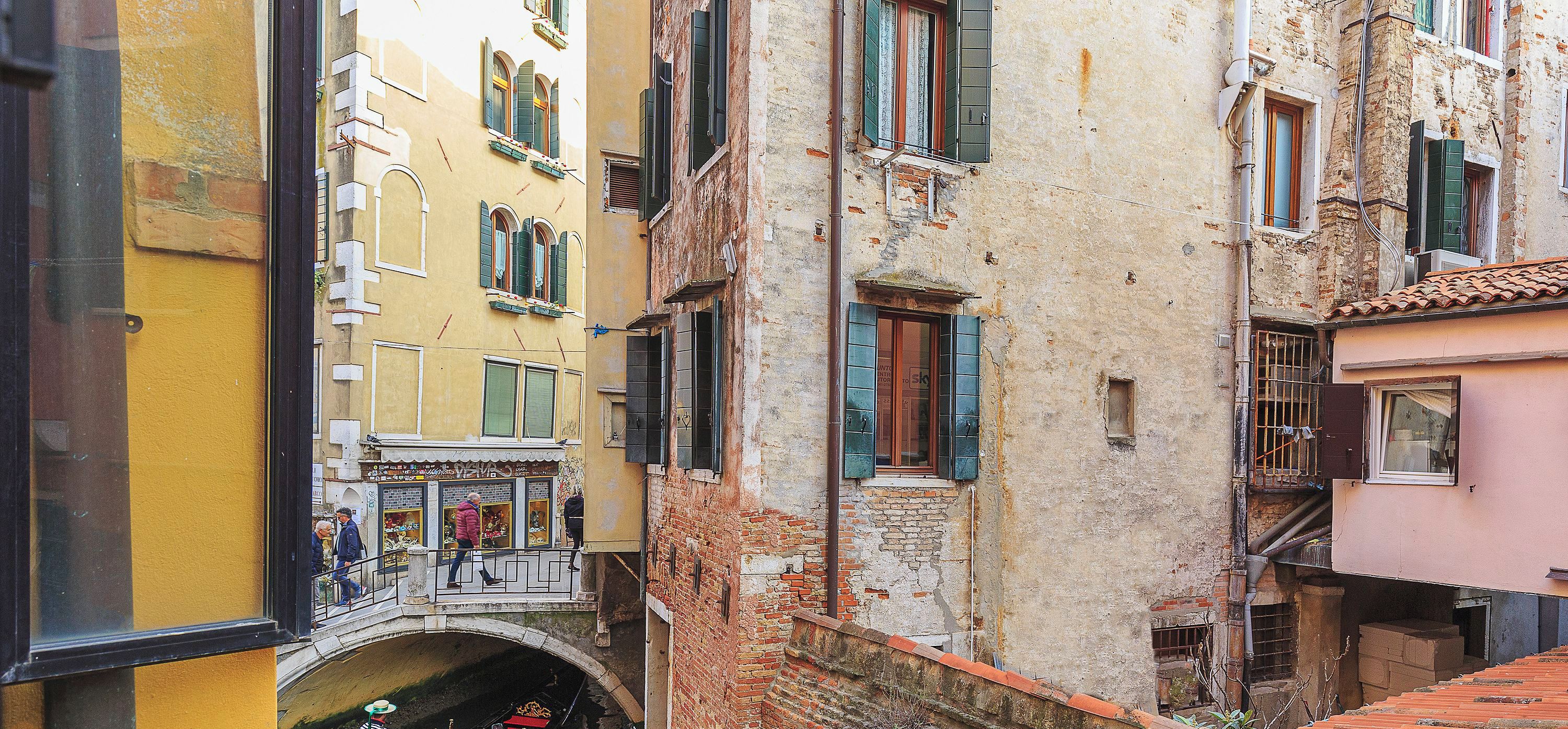 A narrow Venetian canal with a bridge, boats, and buildings.