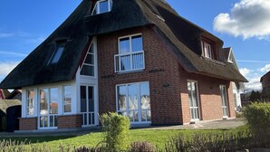 Une maison avec un toit à forte pente, de grandes fenêtres et une façade en briques.
