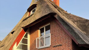 Une maison à deux étages, avec un toit de chaume, des murs en briques et de grandes fenêtres.