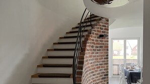 Un escalier avec des marches en bois et un mur en briques, menant à un coin repas où une table est dressée pour deux personnes.