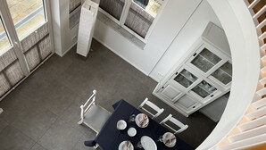 Un coin repas avec une table dressée pour quatre personnes, des chaises blanches et une vue sur l’extérieur grâce à de grandes fenêtres.