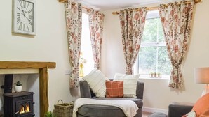 A cozy living room with a fireplace, a sofa, and a window with floral curtains. - Pet-Friendly Country Escape HotTub & Log Burner (Ceredigion)