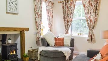 A cozy living room with a fireplace, a sofa, and a window with floral curtains.