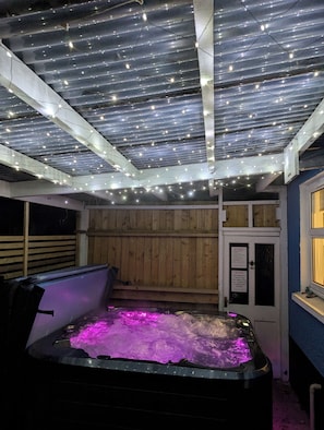A hot tub with purple lighting, surrounded by wooden walls and a ceiling with string lights.