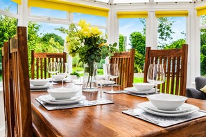 A dining area with a wooden table set for four, surrounded by chairs, with a view of greenery outside. - Synod Cottage | Private Hot Tub, Dog Friendly, Near New Quay (Ceredigion)