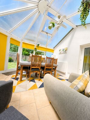 A conservatory with a glass ceiling, wooden dining table, chairs, and a sofa. - Synod Cottage | Private Hot Tub, Dog Friendly, Near New Quay (Ceredigion)