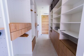 Un pasillo estrecho con estanterías blancas y armarios de madera, que conduce a una puerta de madera al final.