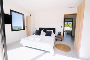 A modern bedroom with a large bed, a TV mounted on the wall, and a view of the outdoors.