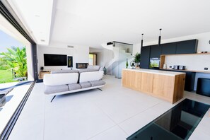 A modern living room with a white sofa, a wooden coffee table, and a kitchen area with dark cabinets and a built-in oven.
