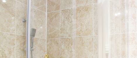 A shower area with a handheld showerhead, a wall-mounted showerhead, and a shelf with toiletries.